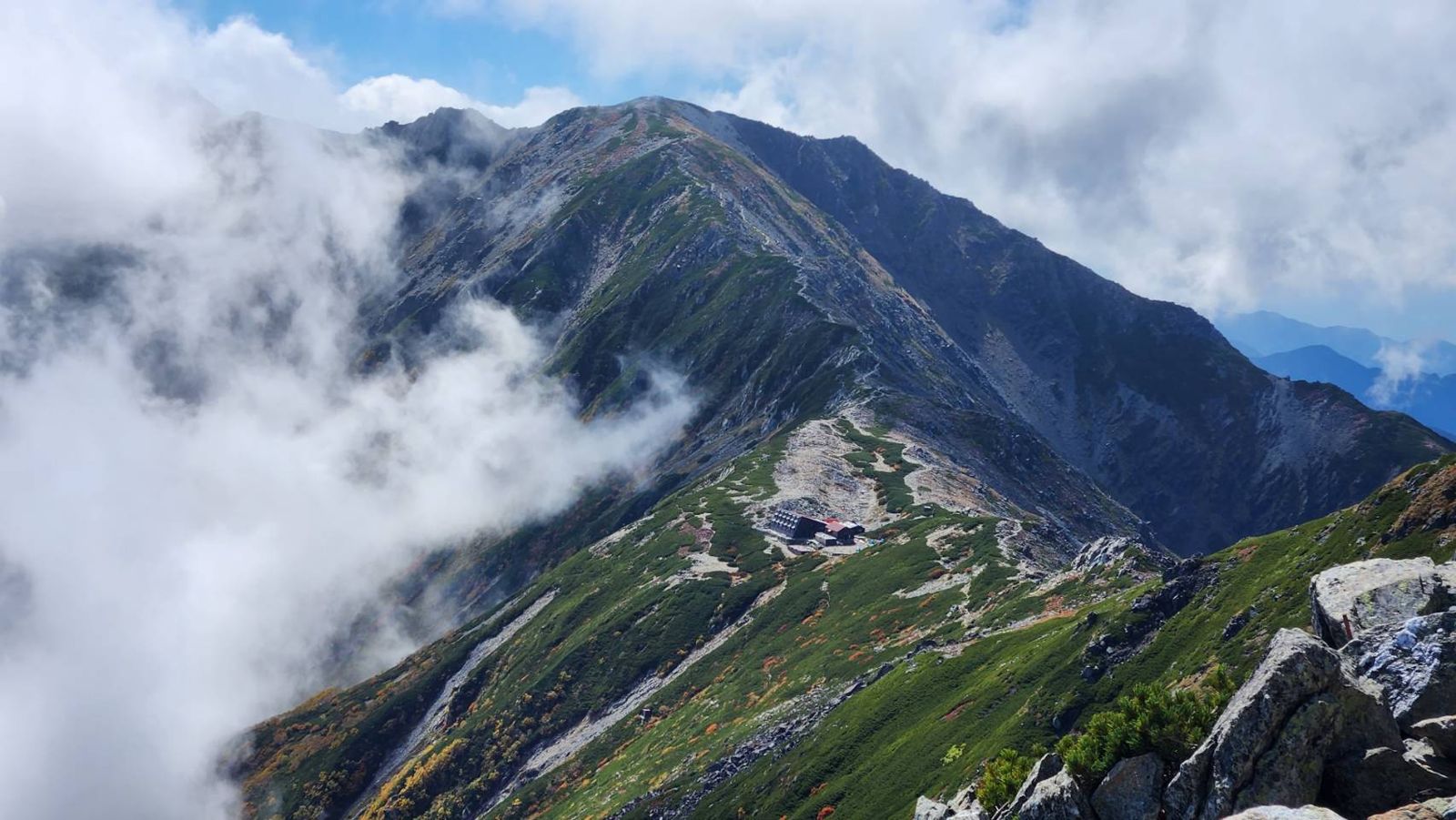 雲の湧く稜線の鞍部に建つ山小屋
